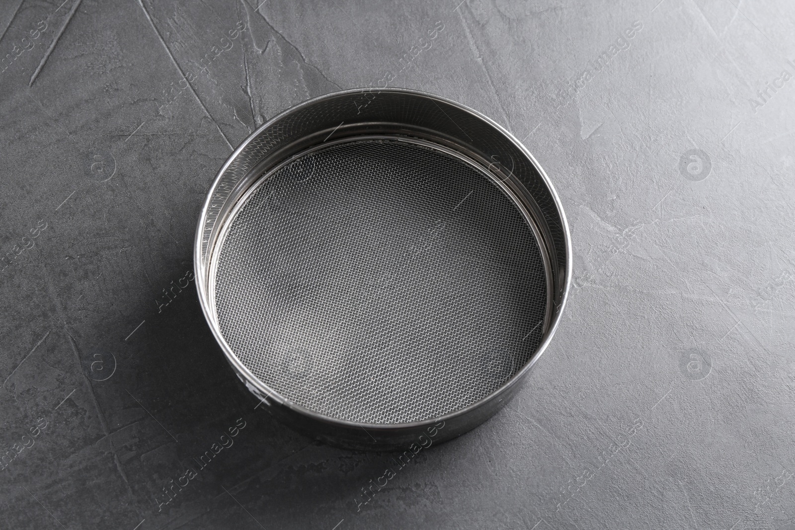 Photo of One metal sieve on grey table. Cooking utensil