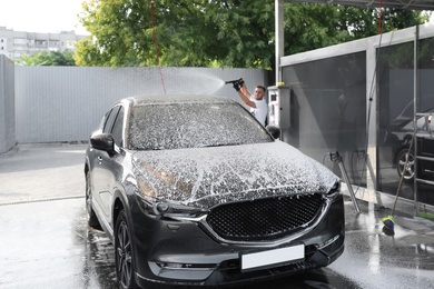 Photo of Young worker cleaning automobile with high pressure water jet at car wash