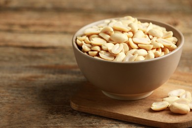 Fresh peanuts in bowl on wooden table, space for text