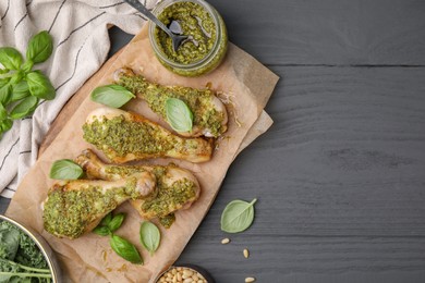 Photo of Delicious fried chicken drumsticks with pesto sauce and ingredients on gray wooden table, flat lay. Space for text