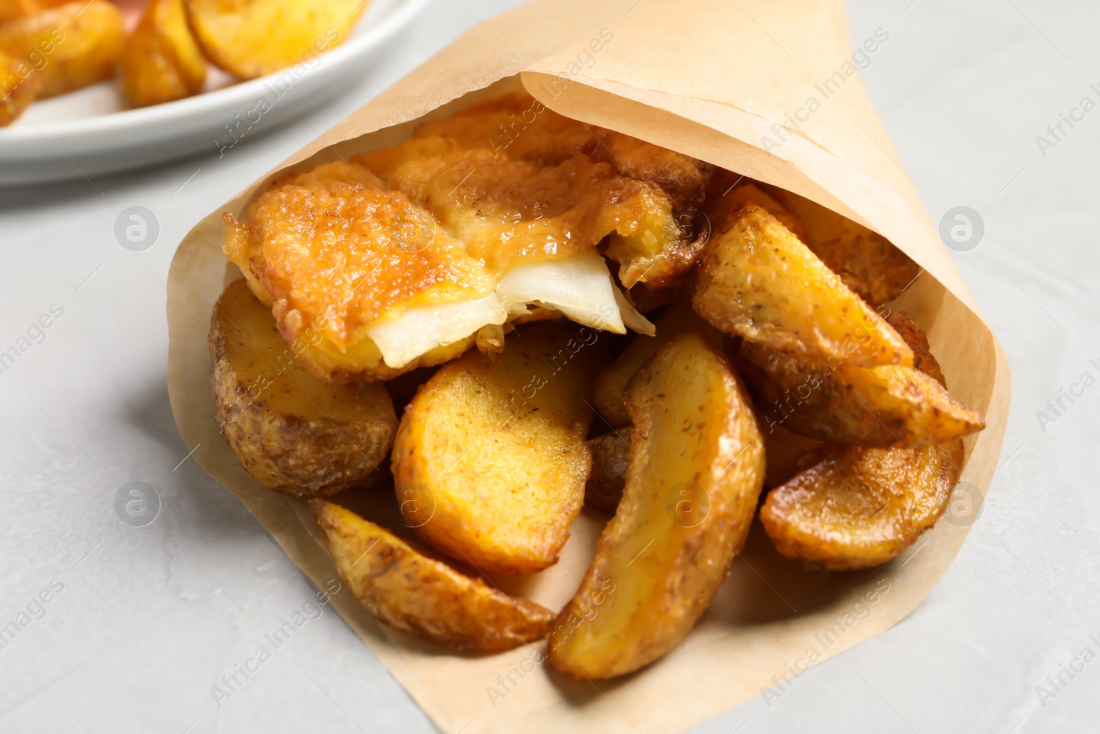 Photo of British traditional fish and potato chips in paper cone on table, closeup