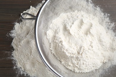 Metal sieve with flour on wooden table, top view