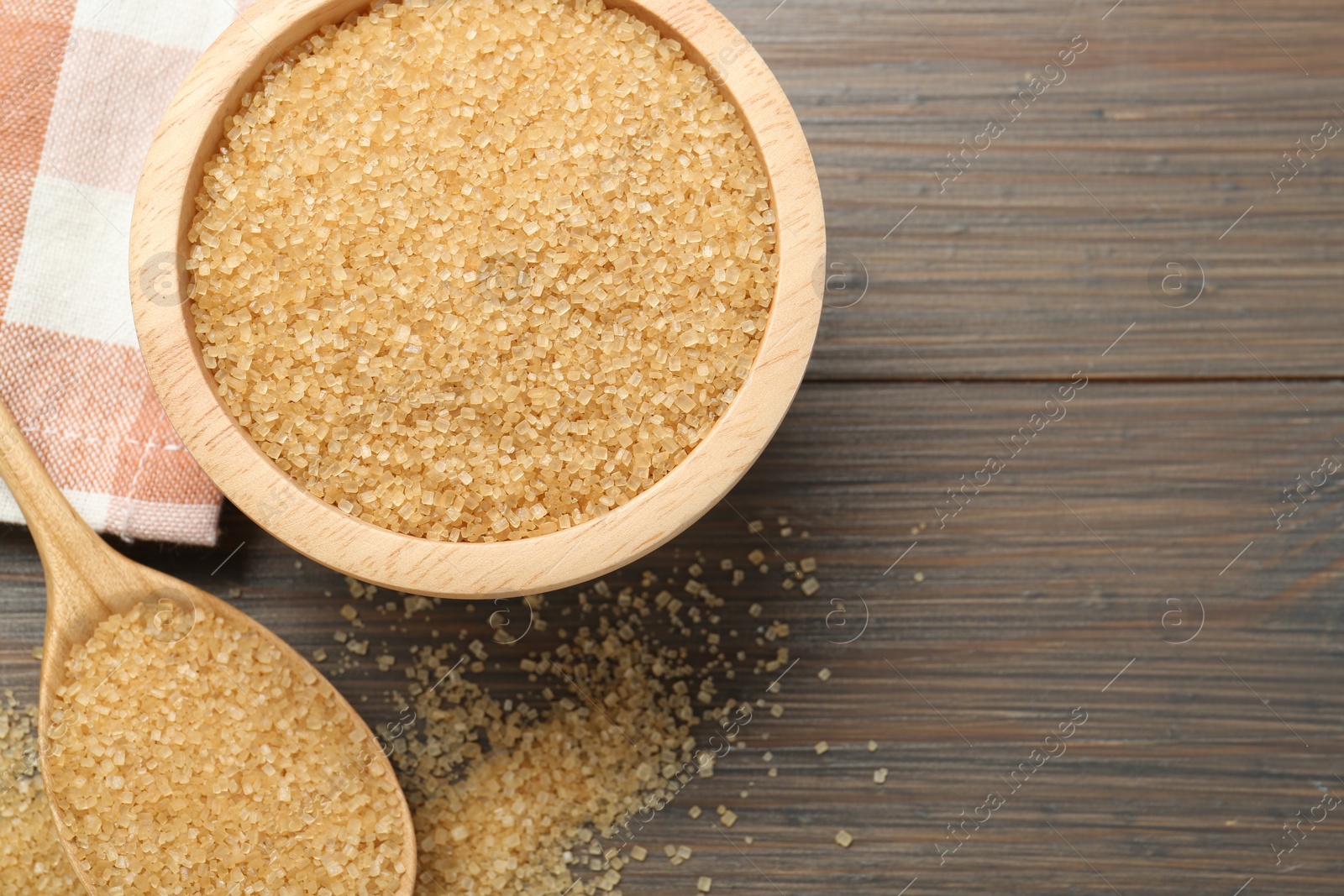 Photo of Brown sugar in bowl and spoon on wooden table, flat lay. Space for text