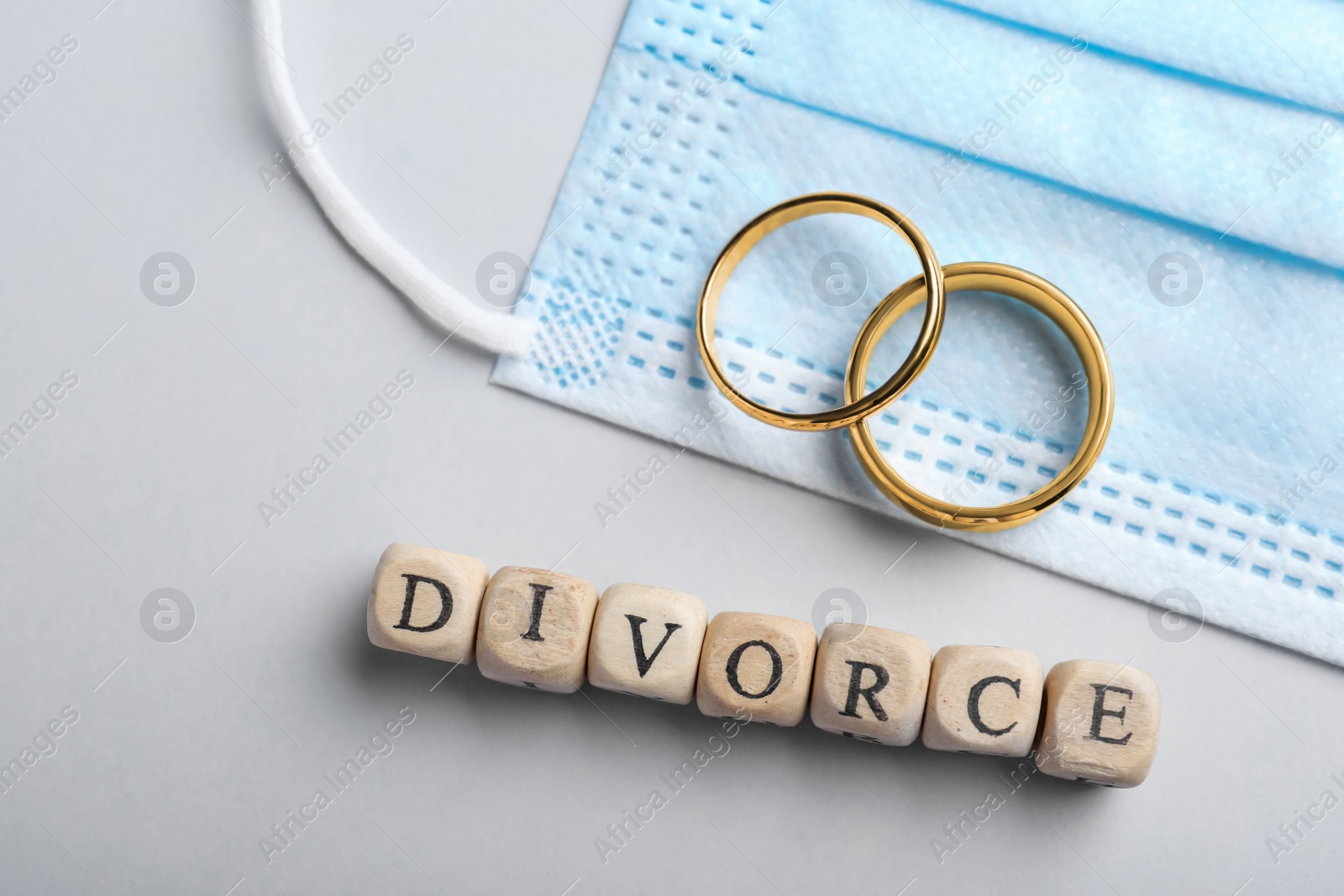 Photo of Wooden cubes with word Divorce, wedding rings and medical mask on grey background, flat lay. Breaking family ties during coronavirus