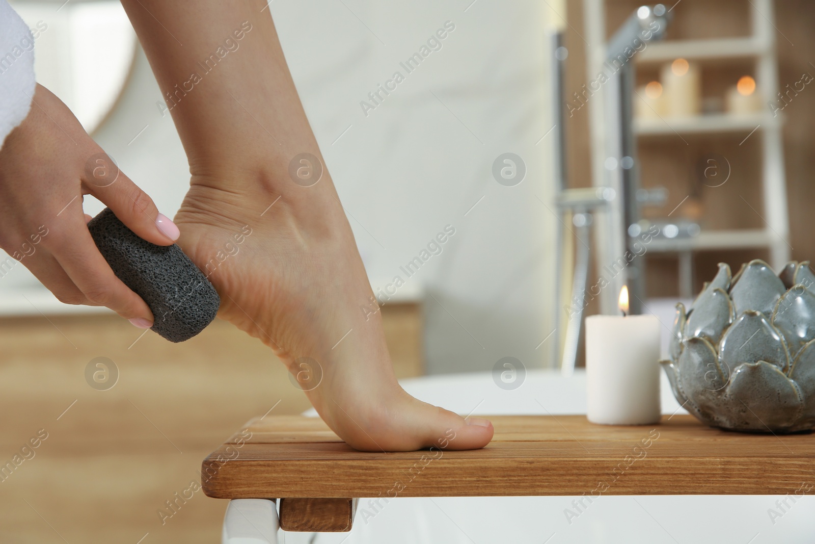 Photo of Woman using pumice stone for removing dead skin from feet in bathroom, closeup