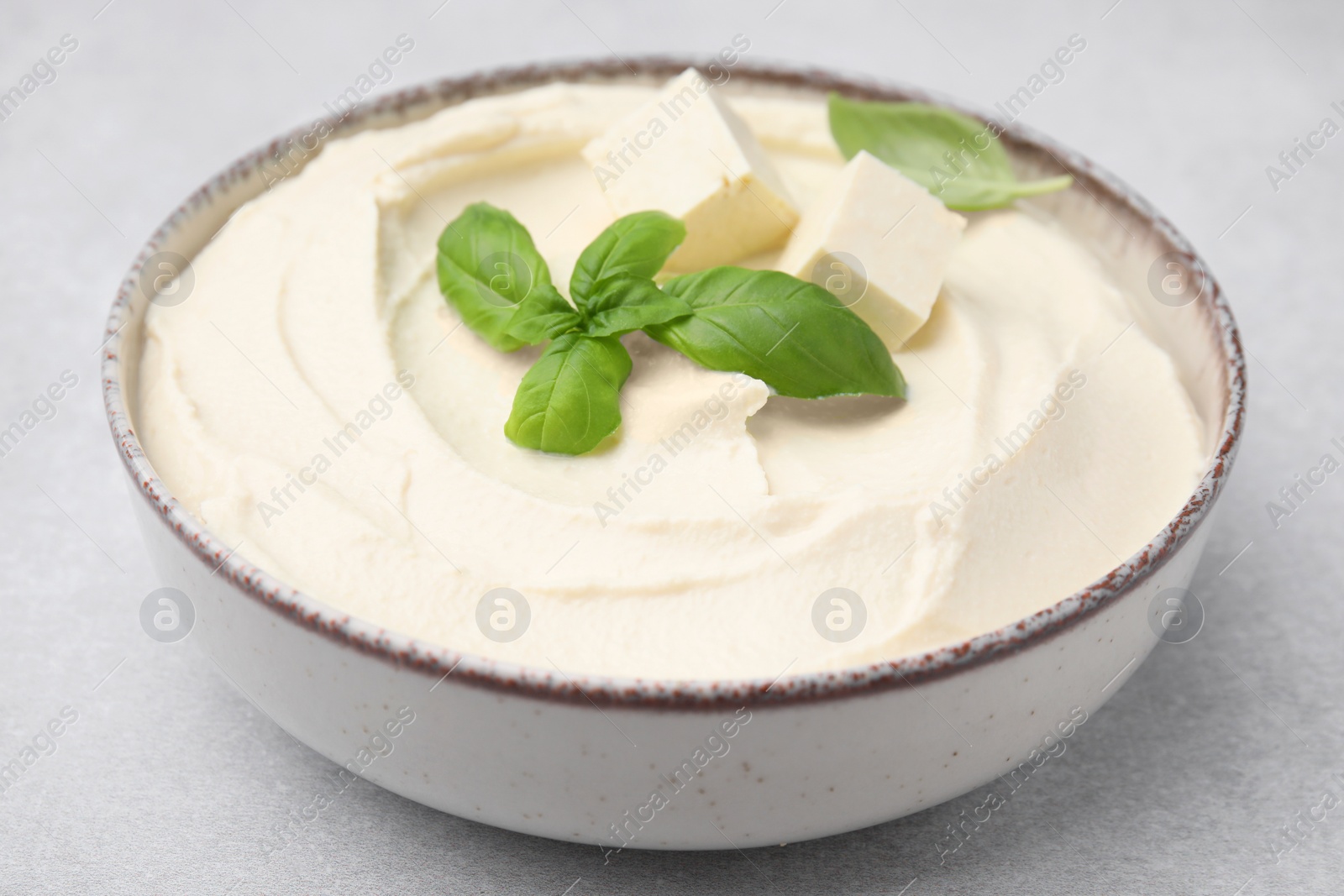 Photo of Delicious tofu sauce and basil leaves on light grey table, closeup