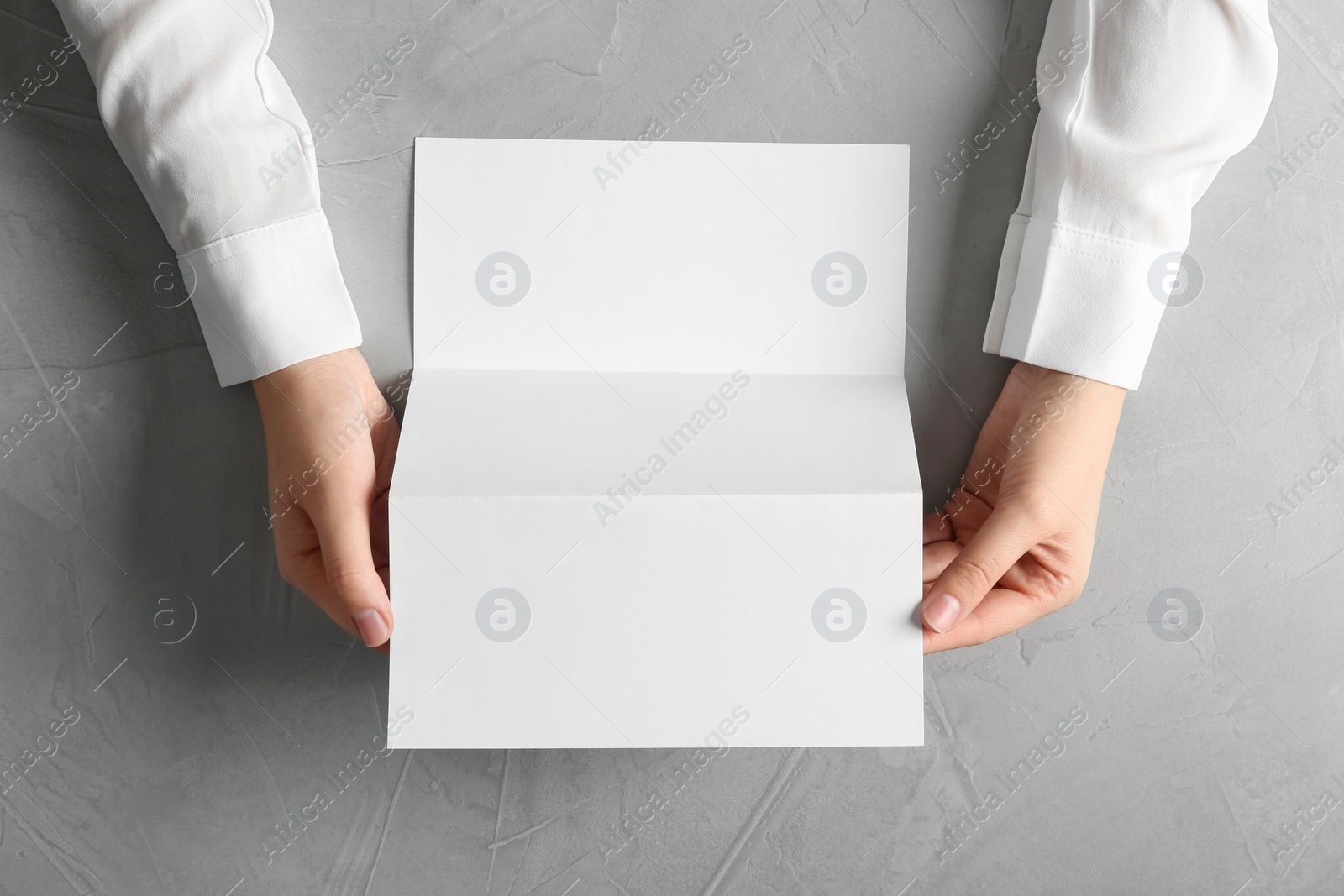 Photo of Woman holding blank brochure mock up on light background, top view