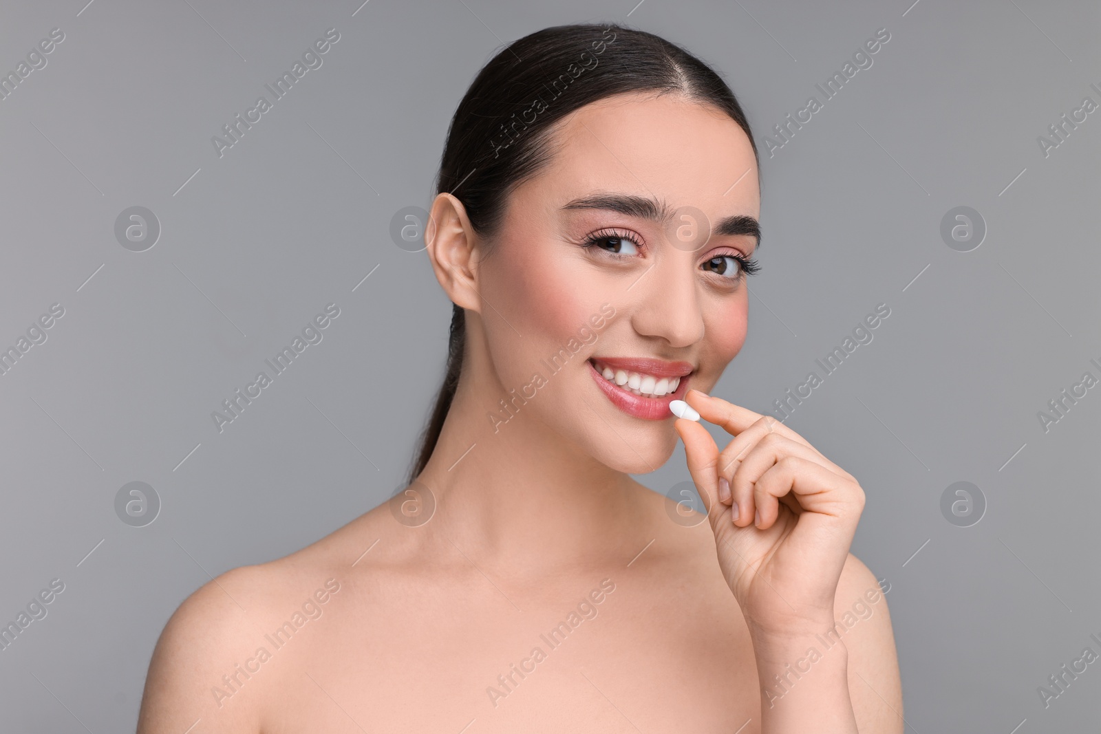 Photo of Beautiful young woman with vitamin pill on grey background