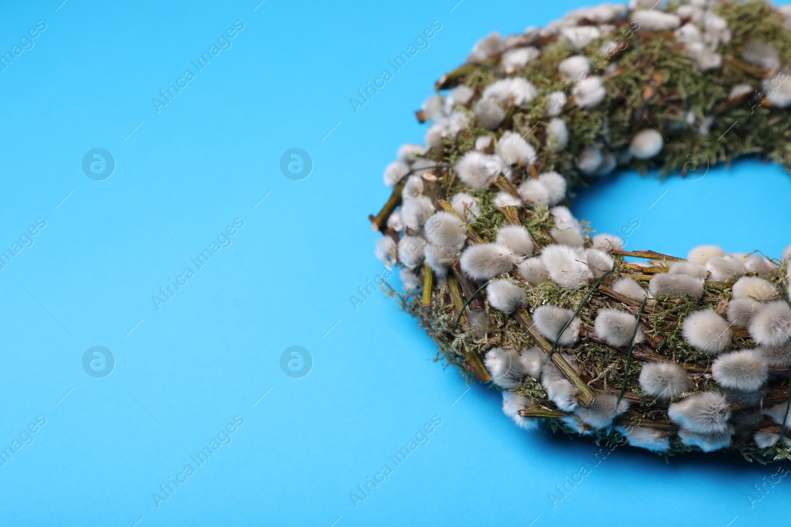 Photo of Wreath made of beautiful willow flowers on light blue background, closeup. Space for text