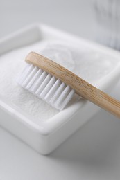 Bamboo toothbrush and bowl of baking soda on white table, closeup