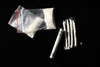 Photo of Drug addiction. Plastic bags with cocaine and rolled dollar banknote on black background,, flat lay