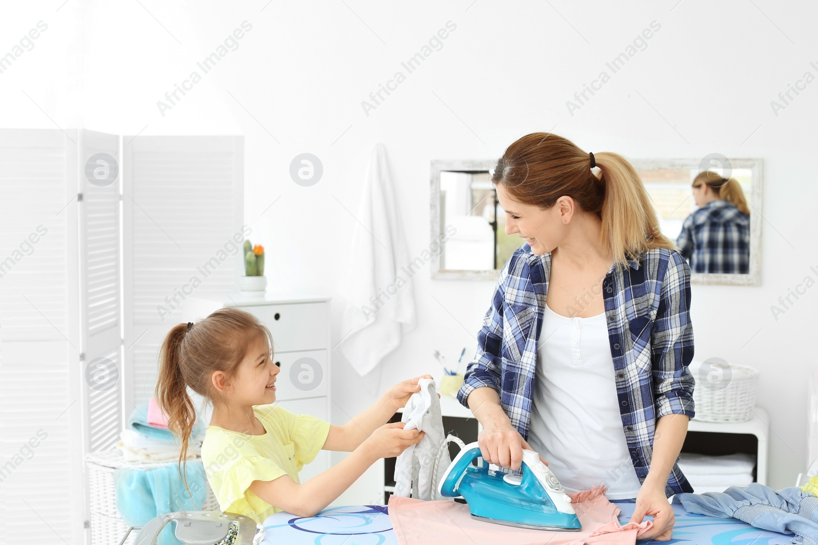 Photo of Housewife with daughter ironing clothes in laundry room