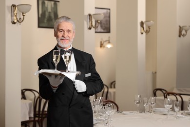 Photo of Senior butler holding tray with glasses of sparkling wine in restaurant. Space for text
