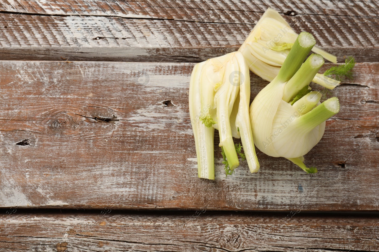 Photo of Whole and cut fennel bulbs on wooden table, top view. Space for text