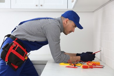 Photo of Electrician with screwdriver repairing power socket indoors