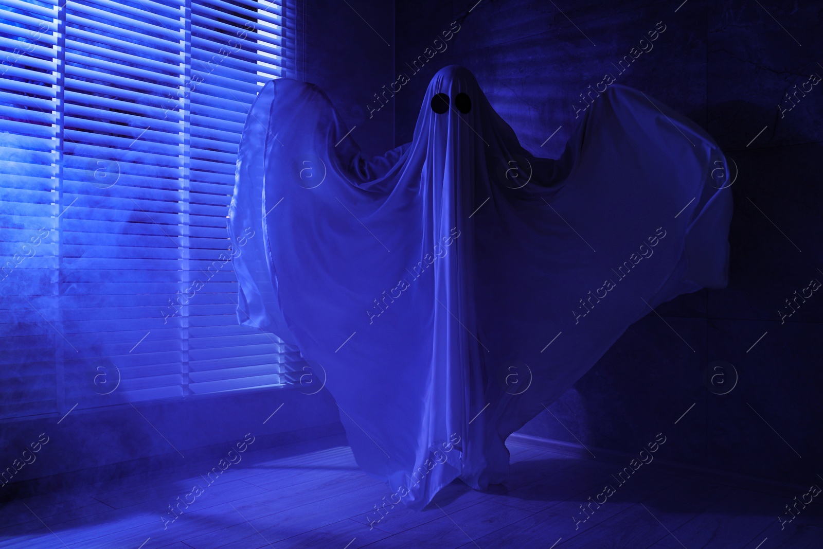 Photo of Creepy ghost. Woman covered with sheet near window in blue light