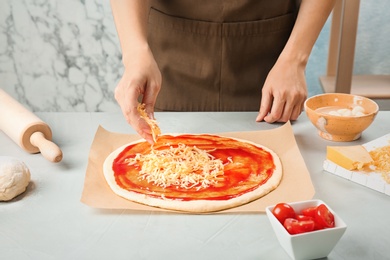 Photo of Woman adding cheese to pizza on table