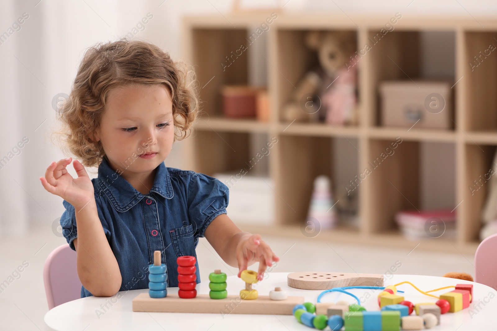 Photo of Motor skills development. Little girl playing with stacking and counting game at table indoors