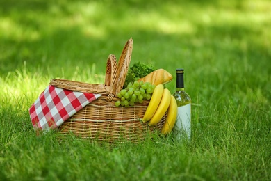 Photo of Wicker basket with blanket, wine and food on green grass in park. Summer picnic