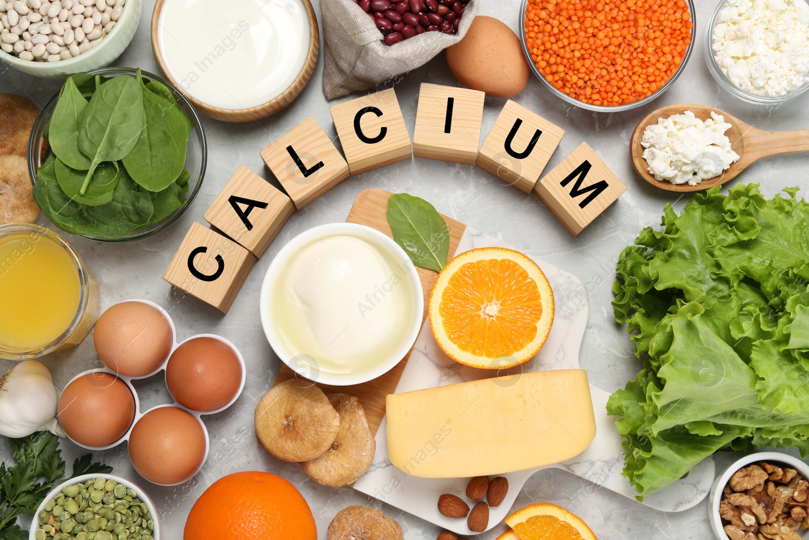 Photo of Set of natural food and cubes with word Calcium on grey marble table, flat lay