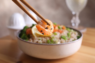 Photo of Chopsticks with shrimp near tasty rice and vegetables on table, closeup