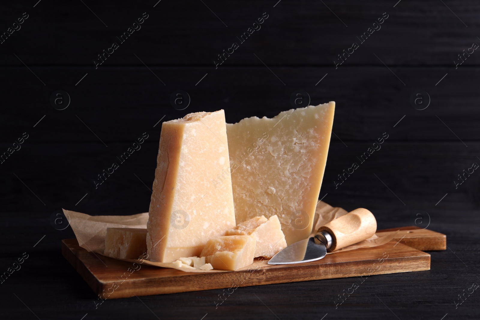 Photo of Parmesan cheese with board and knife on black wooden table