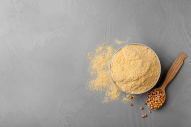 Photo of Bowl with corn flour and kernels in spoon on gray background