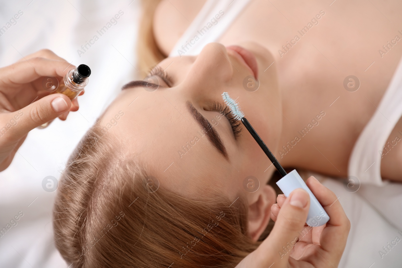 Photo of Beautician applying oil onto woman's eyelashes in salon