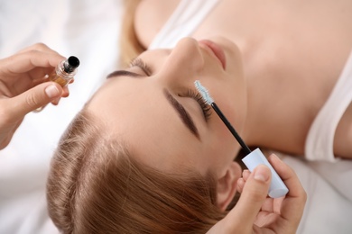 Beautician applying oil onto woman's eyelashes in salon