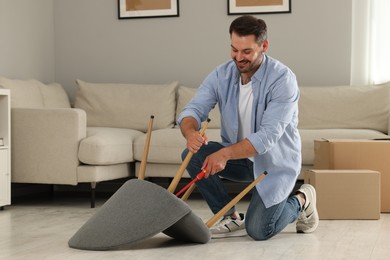 Man with screwdriver assembling armchair on floor at home