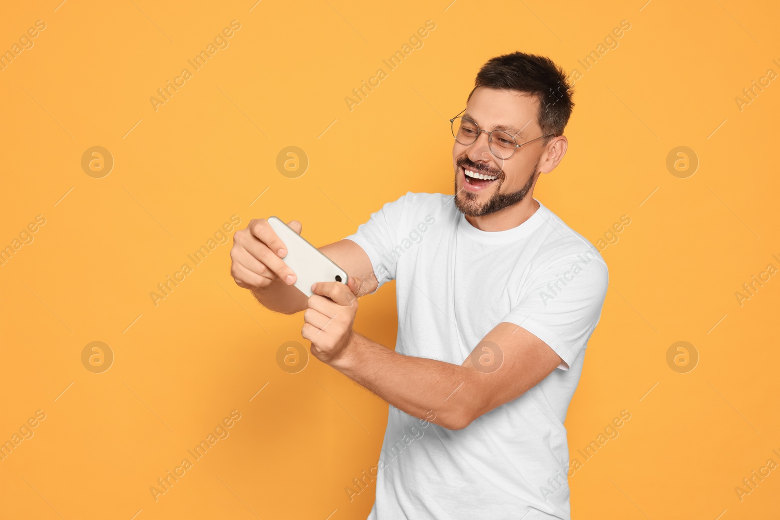 Photo of Emotional man playing game on smartphone against orange background