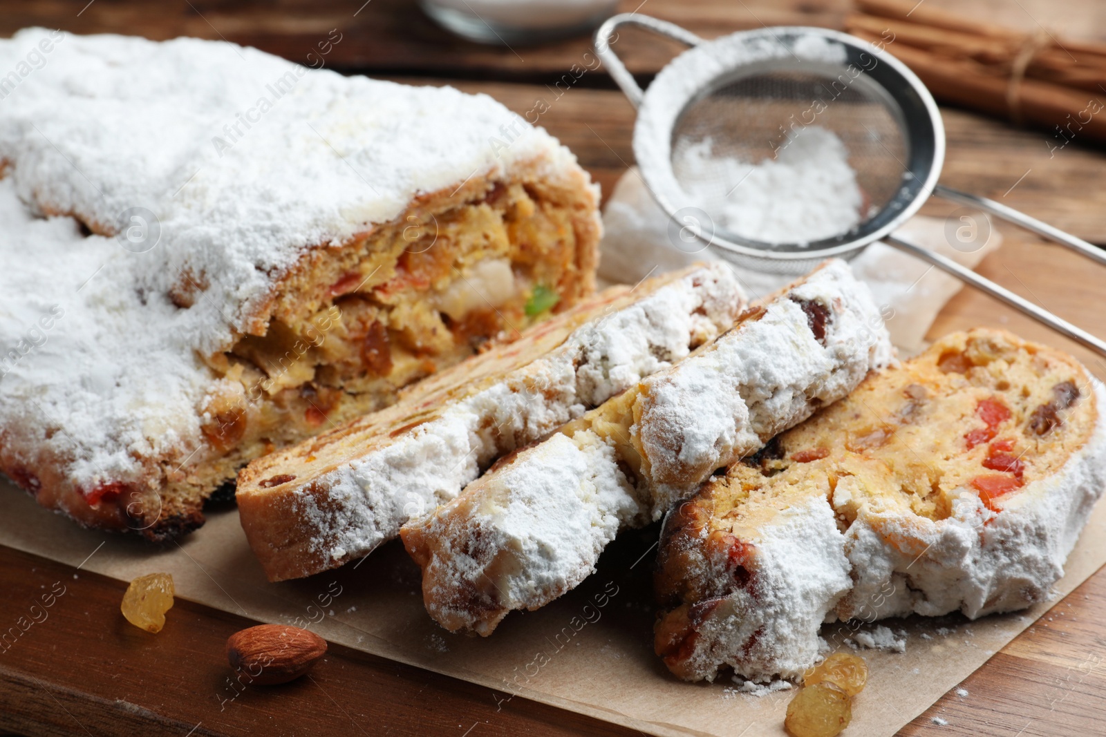 Photo of Traditional Christmas Stollen with icing sugar on wooden board, closeup