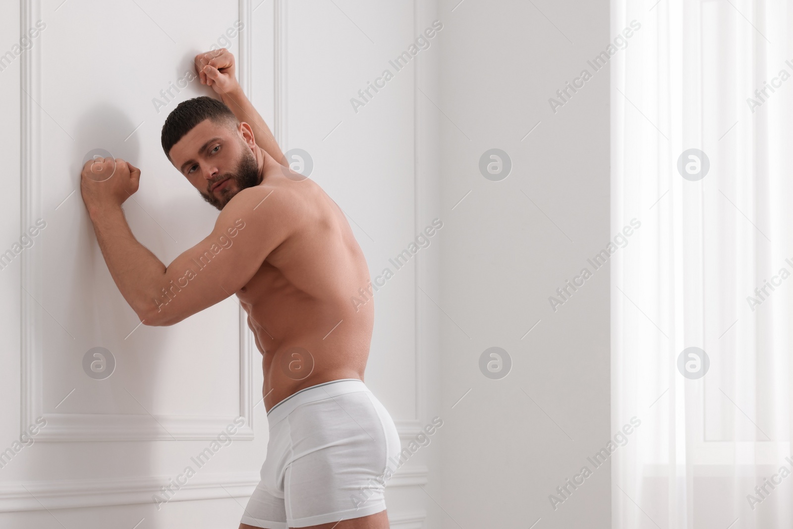 Photo of Young man in stylish underwear near white wall indoors. Space for text