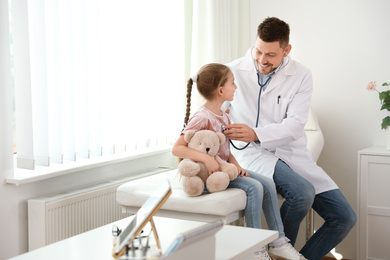 Photo of Children's doctor examining little patient with stethoscope in clinic