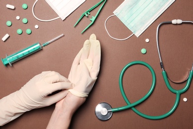 Photo of Doctor in sterile gloves with medical items on color background, top view