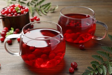 Photo of Tasty hot cranberry tea in glasses and fresh berries on wooden table