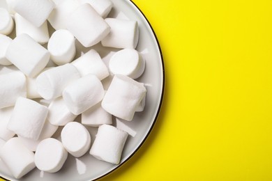 Photo of Delicious puffy marshmallows on yellow background, top view. Space for text
