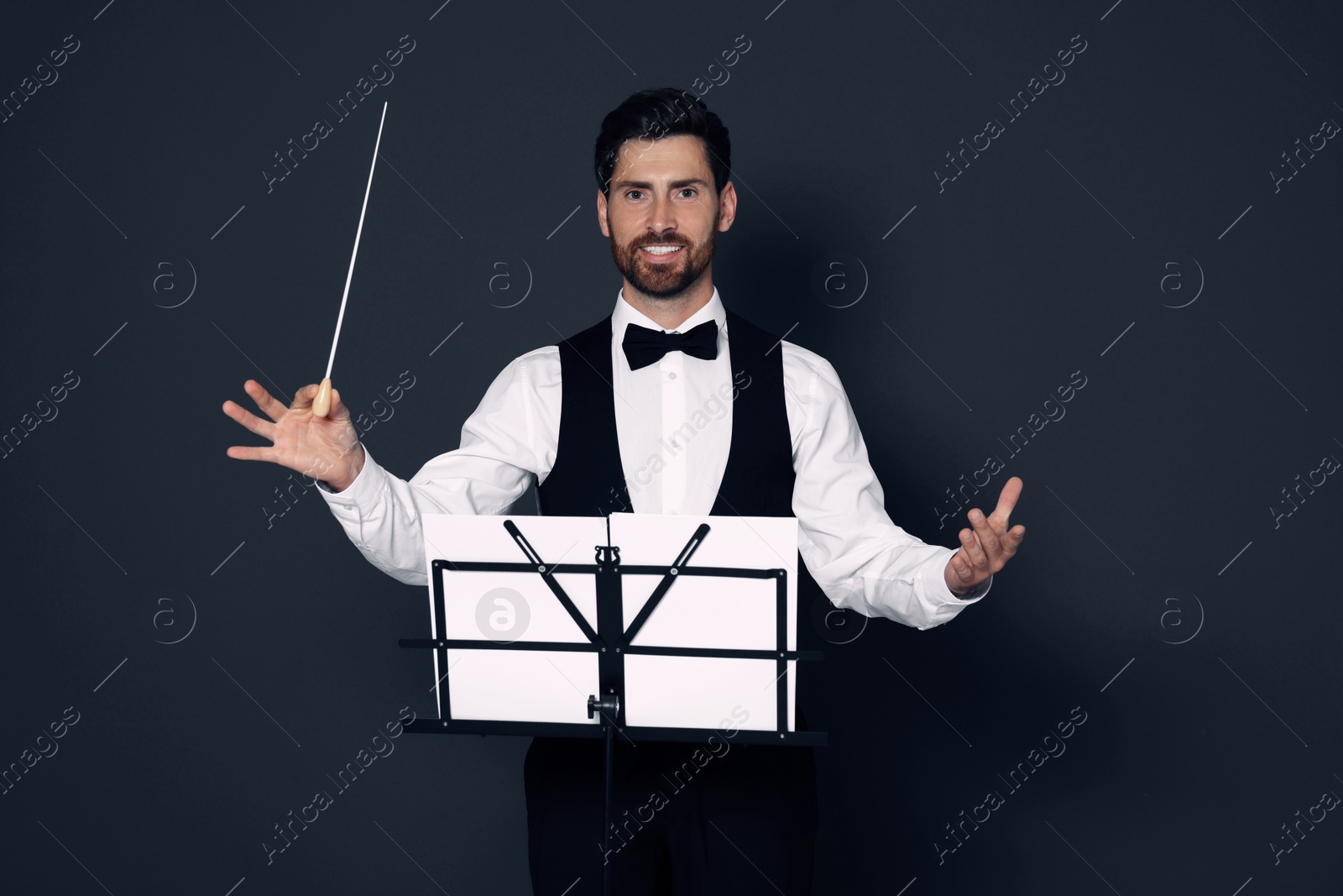 Photo of Happy professional conductor with baton and note stand on grey background