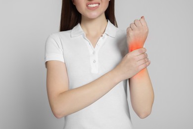 Woman suffering from pain in wrist on grey background, closeup