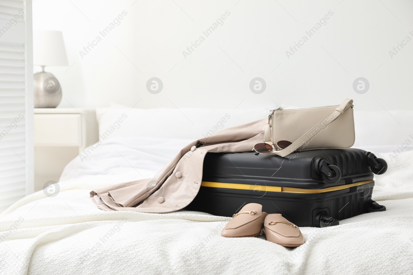 Photo of Suitcase packed for trip, shoes, jacket and fashionable accessories on bed in room