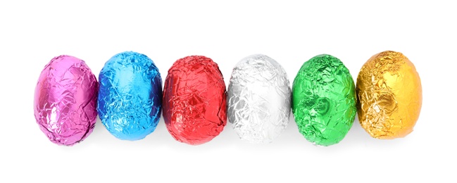 Many chocolate eggs wrapped in bright foil on white background, top view