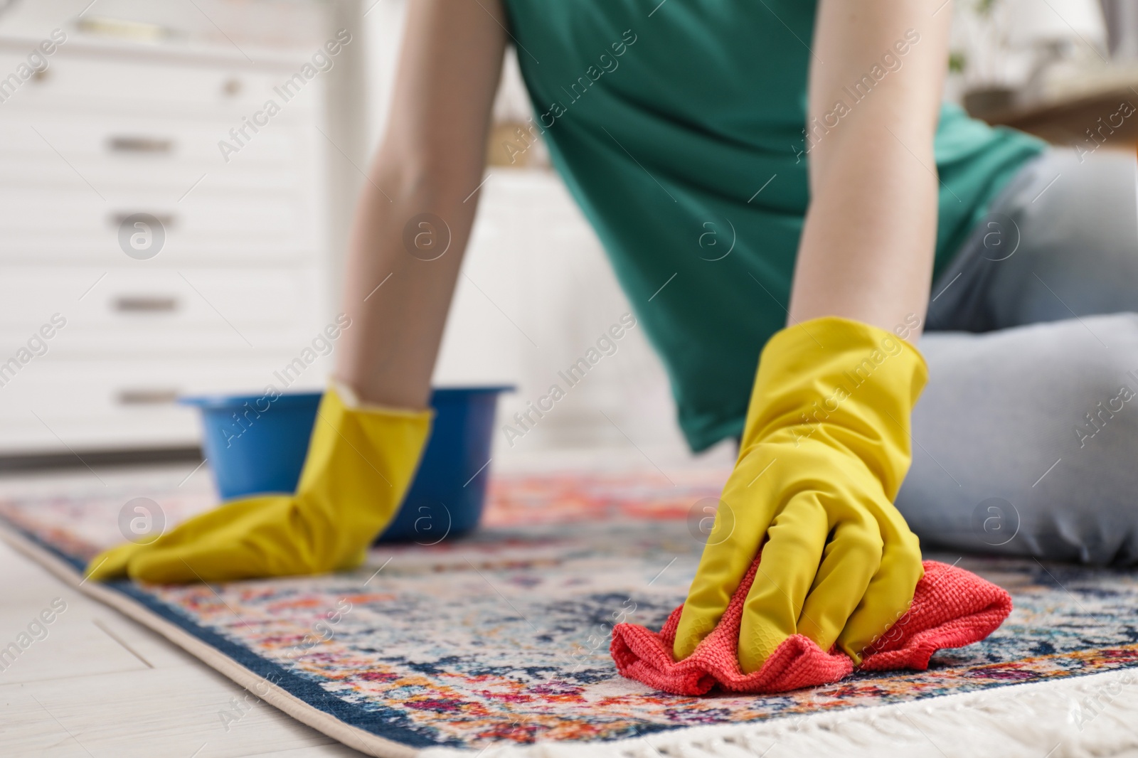 Photo of Woman in rubber gloves cleaning carpet with rag indoors, closeup