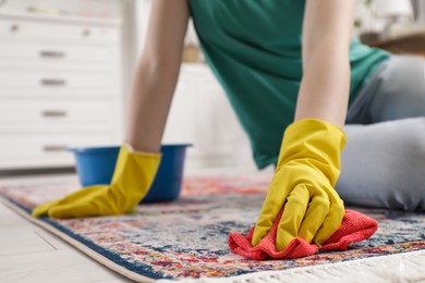 Photo of Woman in rubber gloves cleaning carpet with rag indoors, closeup