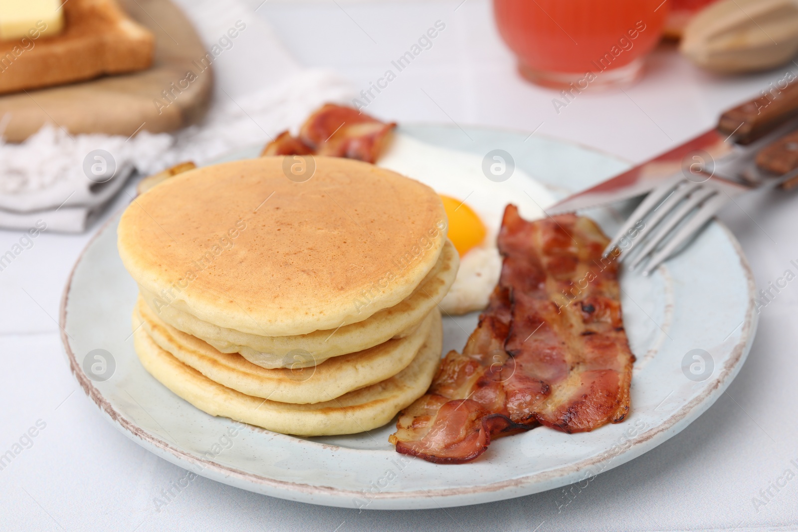 Photo of Plate with tasty pancakes, fried egg and bacon on white table, closeup