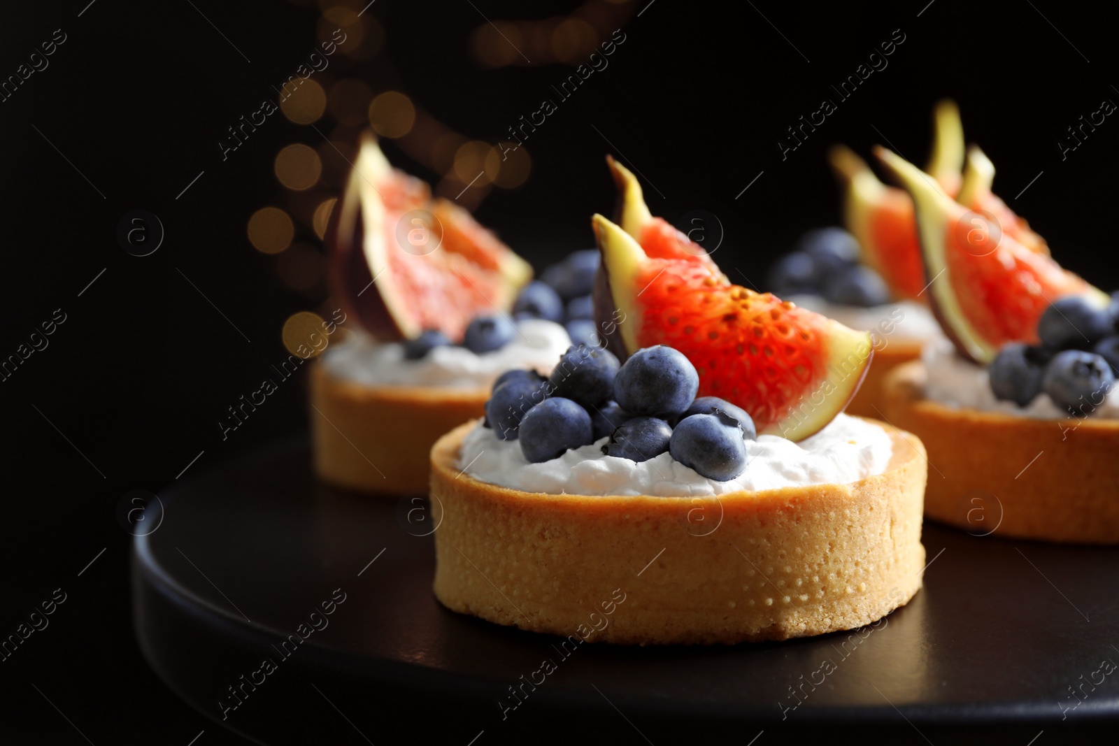 Photo of Tarts with blueberries and figs on black table against dark background, closeup. Delicious pastries