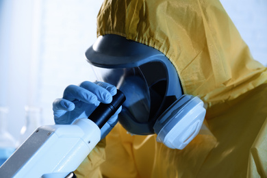 Photo of Scientist in chemical protective suit using microscope, closeup. Virus research