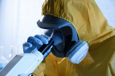 Scientist in chemical protective suit using microscope, closeup. Virus research