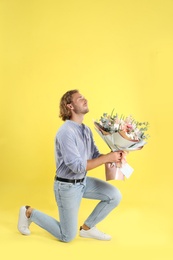 Photo of Young handsome man with beautiful flower bouquet bending knee on yellow background