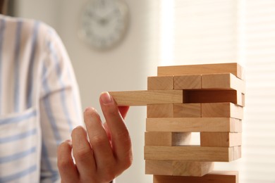 Playing Jenga. Woman removing wooden block from tower indoors, closeup