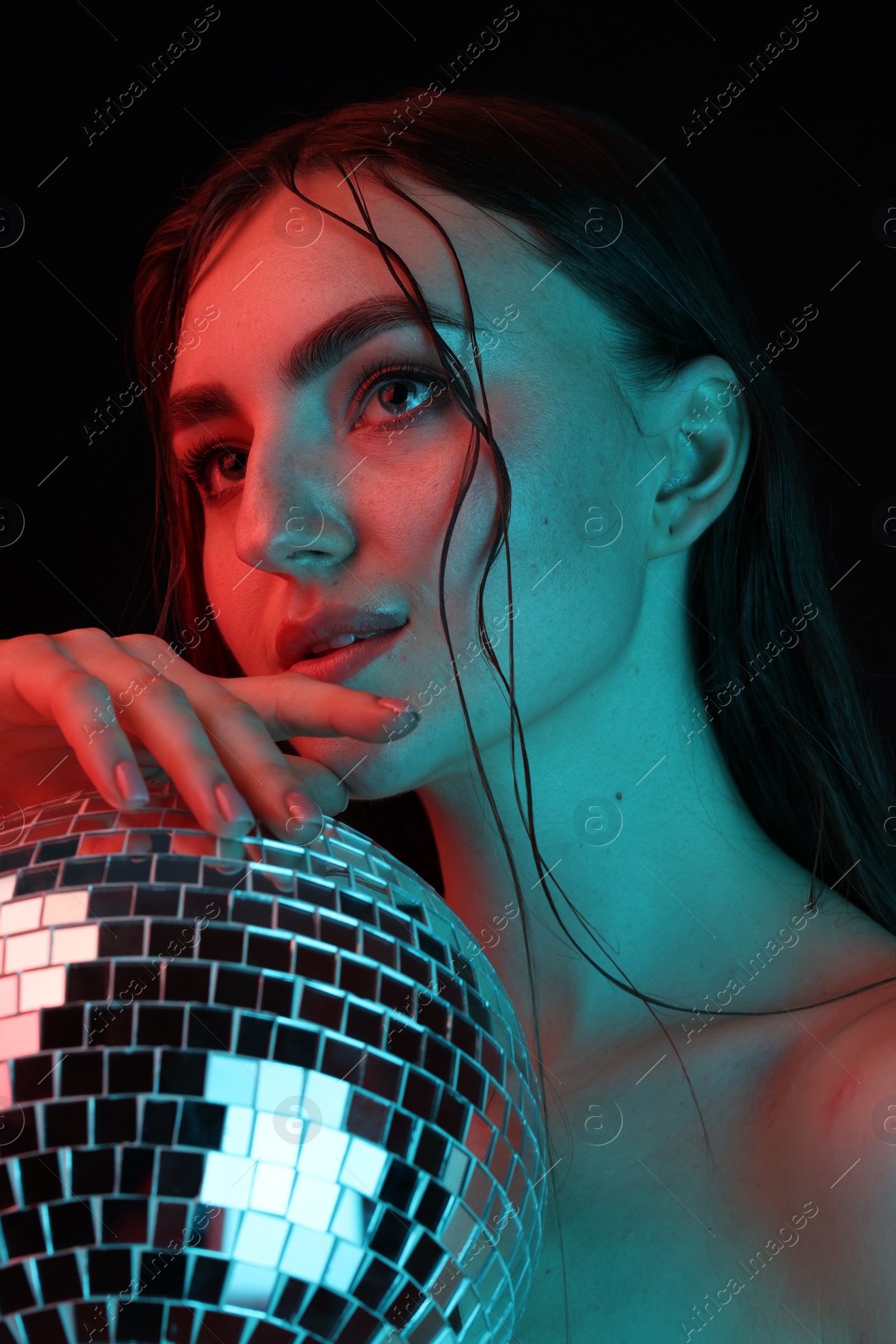 Photo of Beautiful woman with disco ball posing in neon lights against black background